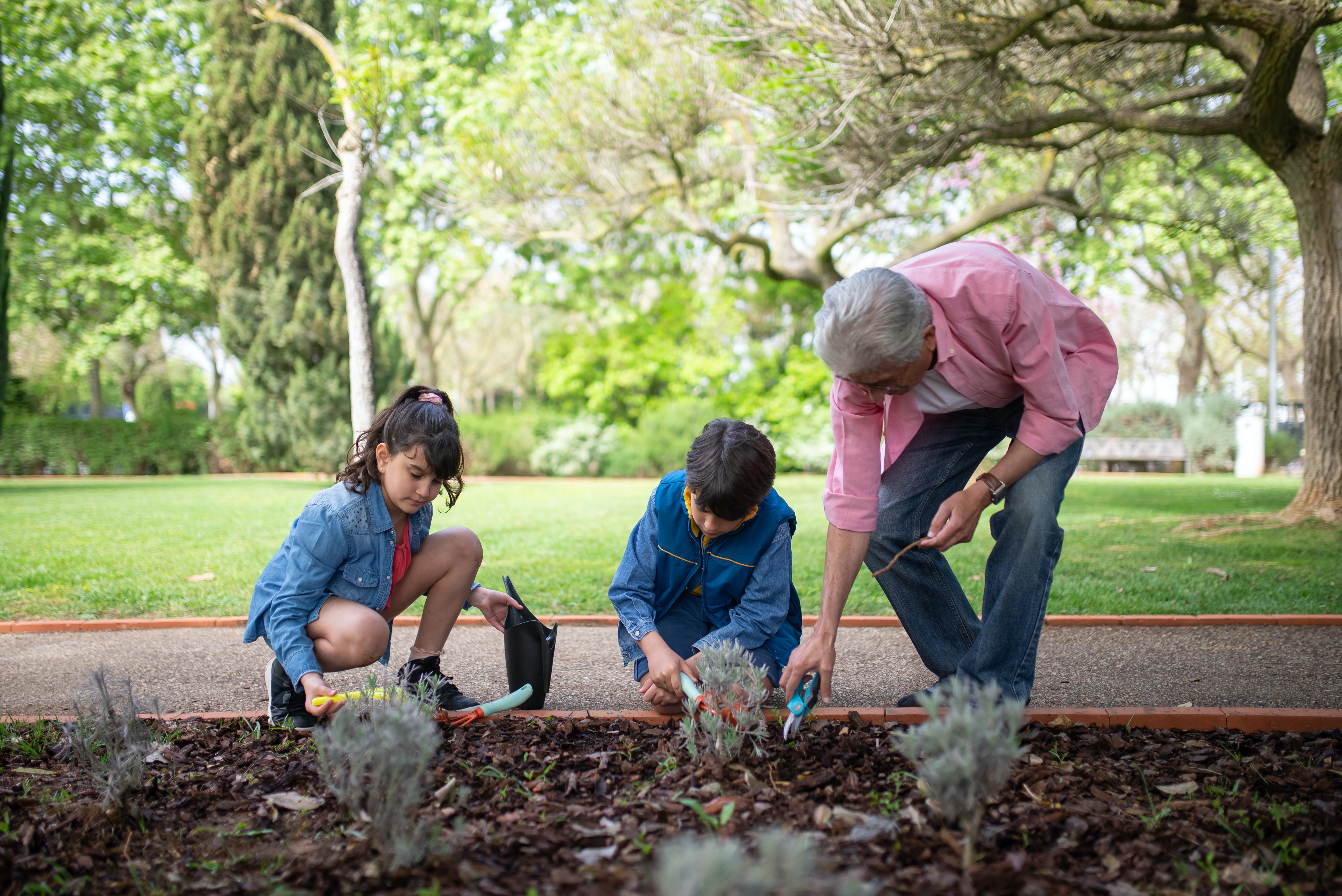 Dos menores haciendo jardinería con hombre mayor